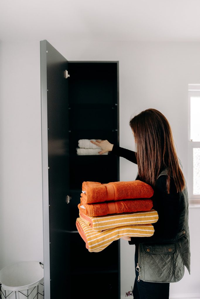 Rebecca putting folded towels into a cupboard, helping a client unpack and settle in quickly after moving house.